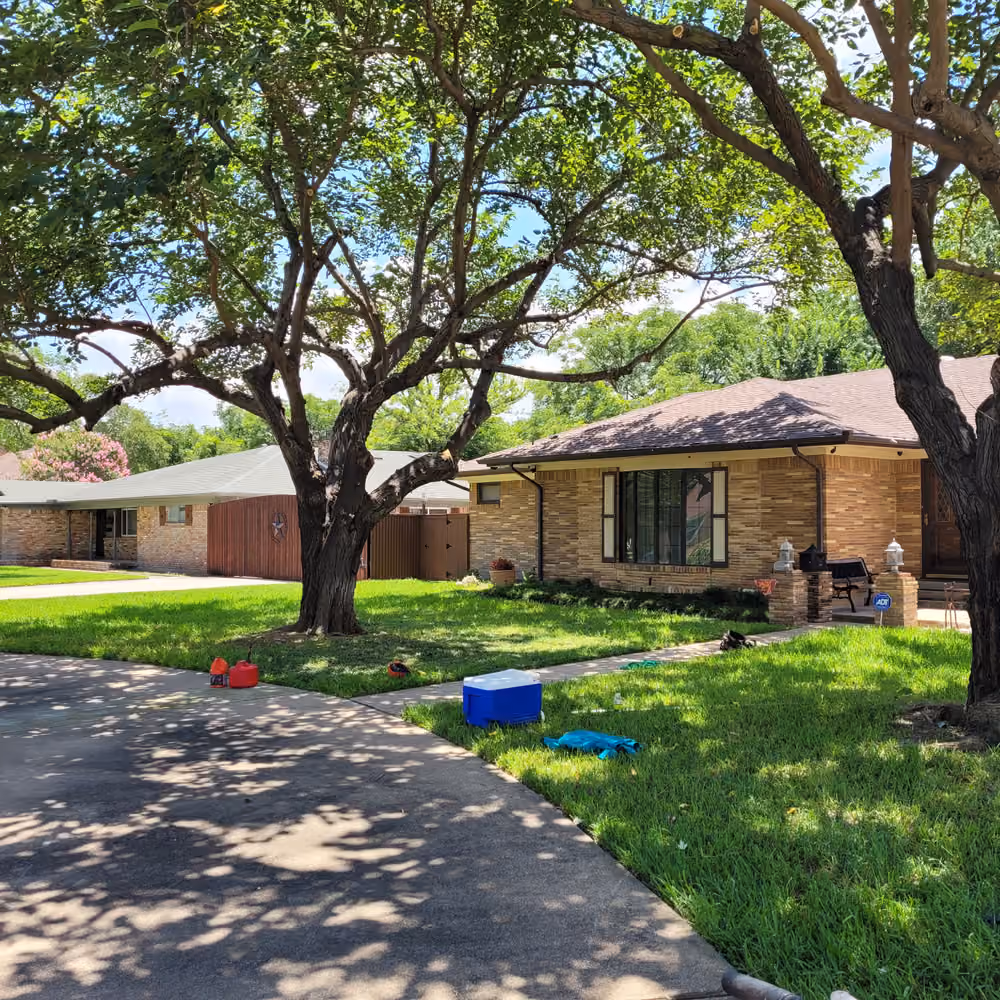 Charming suburban home with lush green lawn and large shade trees on a sunny day.
